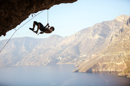 Young man trying to reach cliff in order to continue climbing challenging route. Rock climber pulling himself up and creating rope slack so that belayer could pull in excess rope.の写真素材