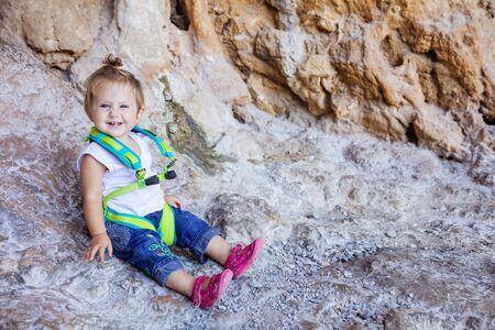 Happy little girl wearing safety harness and sitting at cliffの写真素材