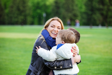 Happy young woman hugging two sons and laughing in parkの写真素材