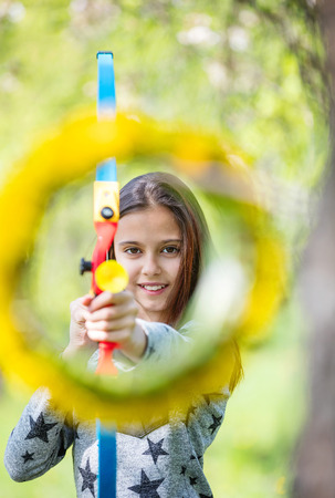 Young girl archer with bow aiming through flower wreath and smiling の写真素材
