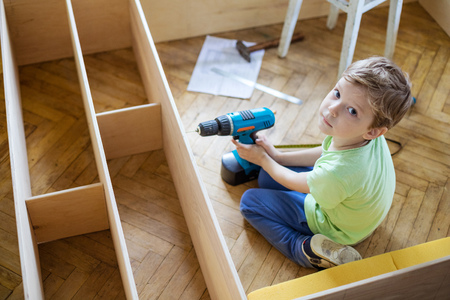 Young boy with screwdriver looking up while sitting on floor at unfinished shelf unit or bookcaseの写真素材