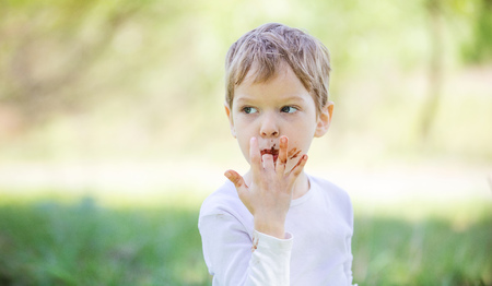 Cute little boy licking fingers while eating chocolate outdoorsの写真素材