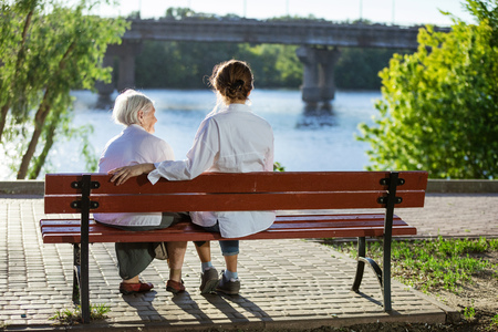 Senior woman and her adult granddaughter sitting on bench in summer parkの写真素材