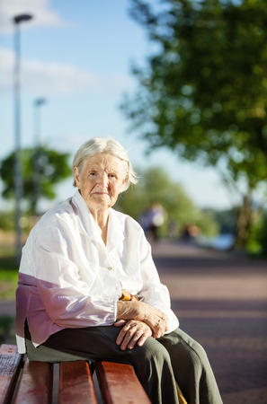 Senior woman sitting on bench in park and smilingの写真素材