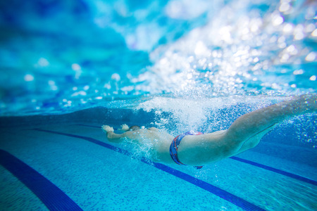 Young man swimming underwater in indoor poolの写真素材