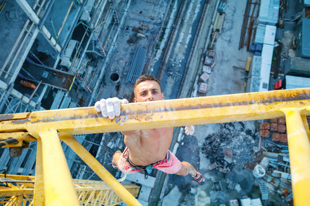 Urban climbing: rock climber hanging on jib of construction crane with one hand, view of construction site belowの写真素材