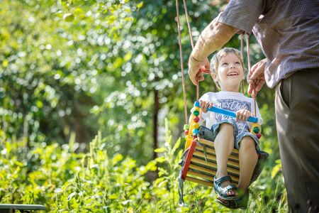 Senior man pushing happy grandson on swing in gardenの写真素材