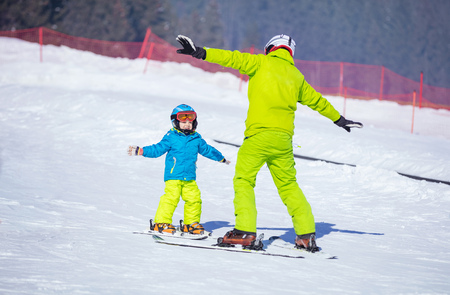 Lesson at skiing school: instructor teaching little skier how to make turns, young boy doing exercise on slope in children's areaの写真素材