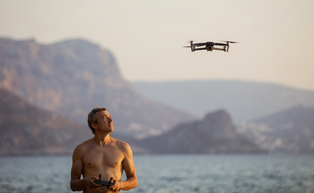 Caucasian man operating drone by remote control at sea shore at sunsetの写真素材
