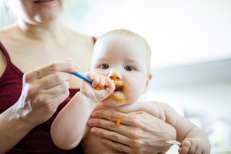 Mother feeding baby girl with spoon at homeの写真素材