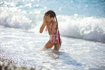 Happy young girl playing on beach in breaking waves and drying her faceの写真素材
