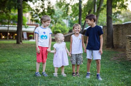 Three young boys and toddler girl in summer park. Friends or siblings having fun outdoors.の写真素材
