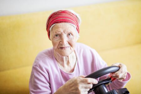 Senior woman enjoying car racing video game while sitting on couch at homeの写真素材