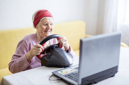 Senior woman enjoying car racing video game on laptop while sitting on couch at homeの写真素材