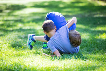 Two boys fighting outdoors. Siblings or friends wrestling on grass in summer park. Siblings rivalry.
