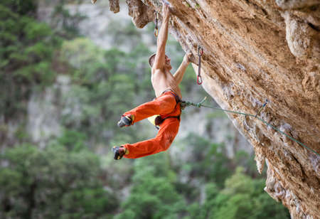 Young male rock climber after jumping and gripping small handholds on overhanging cliffの写真素材
