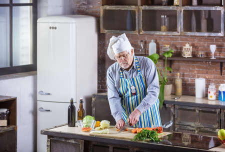 Senior man in chef hat chopping fresh vegetables for salad. Healthy eating habits.