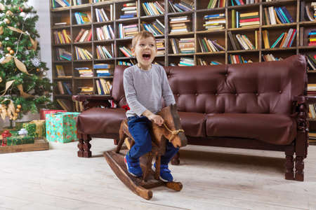 Happy preschool boy on wooden rocking horse, with Christmas tree in backgroundの写真素材