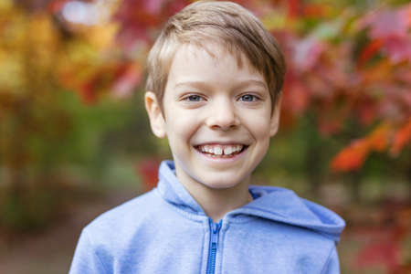 Cute young boy smiling on walk in autumn park, closeup portraitの写真素材