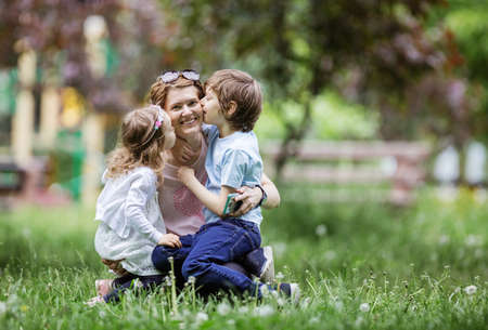 Young kids kissing mom while playing in summer parkの写真素材