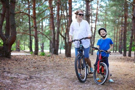Cheerful mother and son riding a bicycle in a forestの写真素材