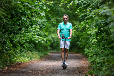 Caucasian blonde man riding electric scooter on road in parkの写真素材