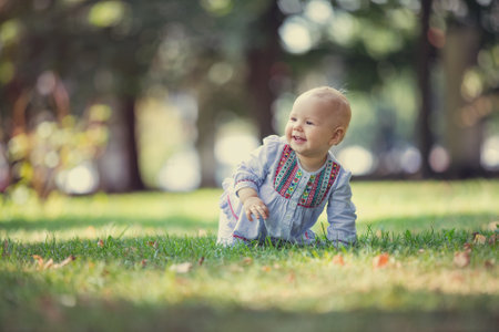 Cute baby girl crawling on lawn in park in summer
