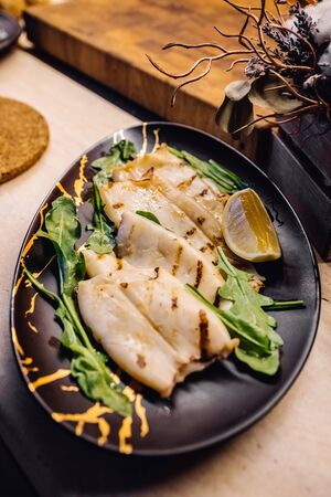 Fried calamari on black plate at home kitchen. Roasted squid laying on wooden deck at kitchen.