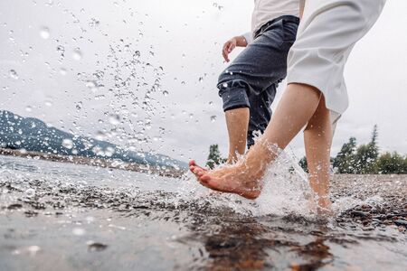 Two people walking with naked legs on river shore. Pebbles under bare foot and cold water of river.の写真素材