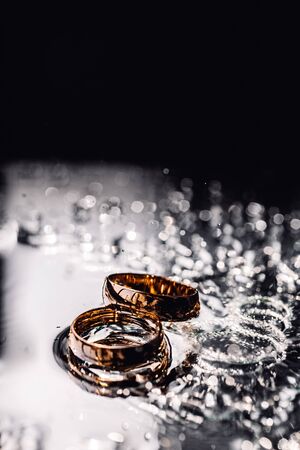 Two wedding golden rings in water splashes laying on flat surfaceの写真素材