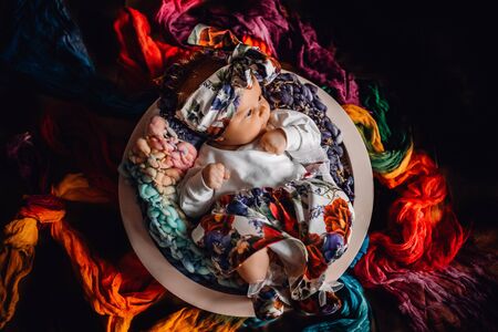 Newborn baby on black background. Little caucasian baby laying on colourful fabrics