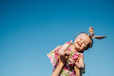 Baby in air. Cheerful child in blue sky background. Infant girl on hands flying in clouds. Fashion child with headwearの写真素材
