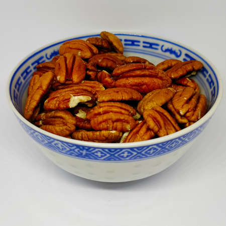Detail view on pecan nuts in the Chinese porcelain bowl on the white background.