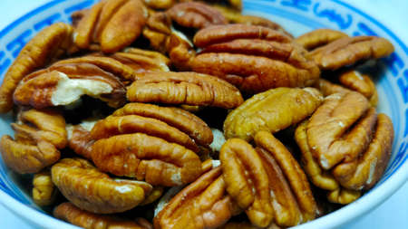 Detail view on pecan nuts in the Chinese porcelain bowl on the white background.
