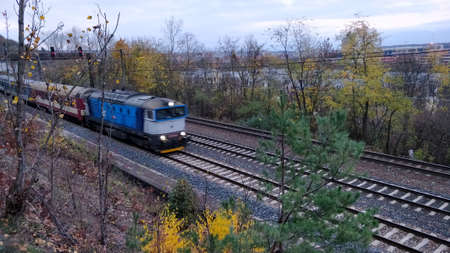 Blue passenger train moves on railroad in Prague suburb. In the background are Autumn trees. The railroad consist of three tracks.のeditorial素材