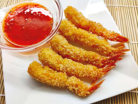 Five shrimp tempura pieces and sweet chilli sauce served on the white plate and bamboo mat. This traditional Portuguese and now Japanese food is delicious and crispy.の写真素材