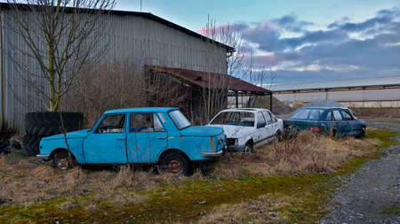 Wrecks of red, white and dark blue cars parked in an old scrapyard.