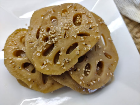 Detail of cooked lotus rhizomes in soy sauce with sesame seeds served on white plate.の写真素材