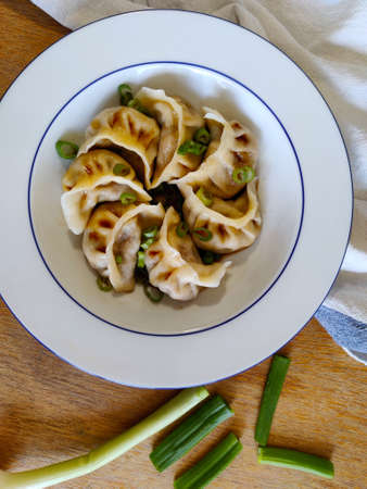 Chinese dumplings called jiaozi with spring onion and soy sauce served in white plate. There are table cloth and whole spring onion around the plate as a decoration.の写真素材