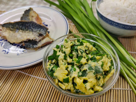 Scrambled eggs with spring onion in transparent bowl. There are two fish fillets on the left side and bunch of spring onion with bowl of jasmine rice on the right side.の写真素材