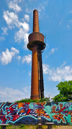 Prague, Czech Republic - June 19, 2021: Abandoned old red tall industrial chimney in the brownfield...