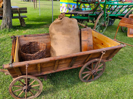 Traditional old wooden cart with wicker basket and sack full of something. The cart stands on the...