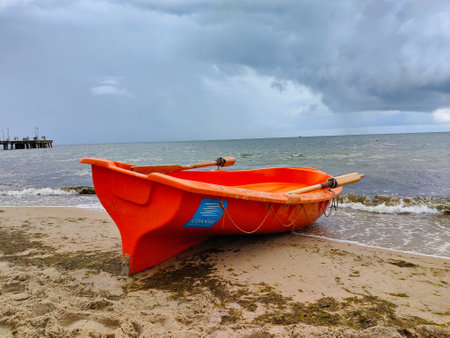 An orange rescue lifeboat prepared for action on the sandy beach of Poland Baltic sea. The weather is rainy and the water is calm.の写真素材