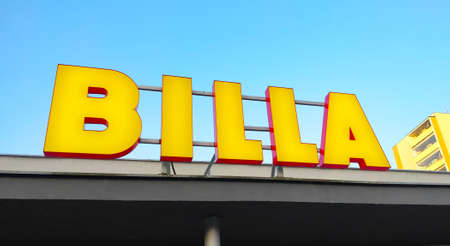 Prague, Czech Republic - September 8, 2021: Yellow logo of supermarket chain Billa fixed on the roof of the building with blue sky in the background.のeditorial素材