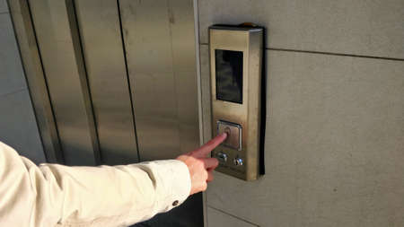 A person is pressing a button of an elevator using index finger. Control board and elevator door are...