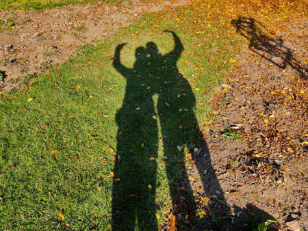 Silhouette of two people making a heart shape with their hand on the autumn grass in front of them.の写真素材