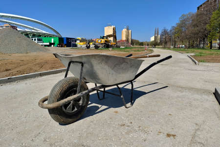 Detail of old metal construction wheelbarrow standing on the unfinished sidewalk.