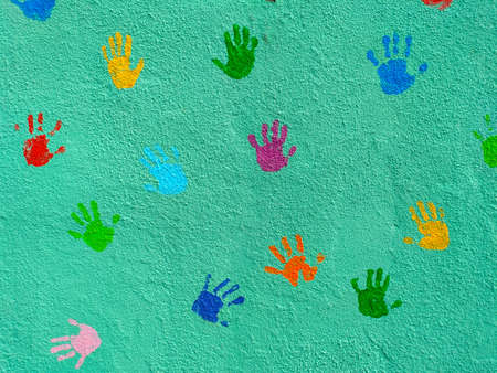 Colorful children hands painted on a green wall. There are yellow, green, purple, blue, orange,...