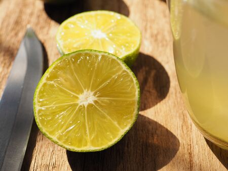  Close up fresh limes sliced in half on a wooden table with a knife and glass, High Vitamin C, Detox...