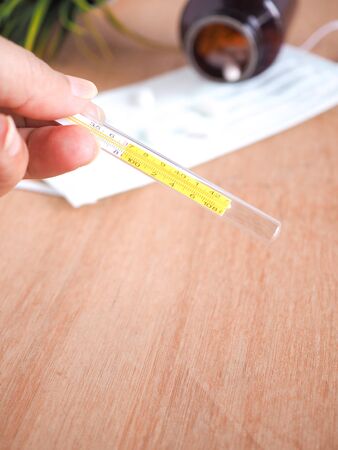 A woman's hand holding a thermometer on a wooden table in the house.の写真素材